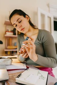 Young woman using glucometer while doing homework at home