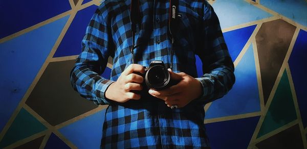 Low section of man photographing against blue wall