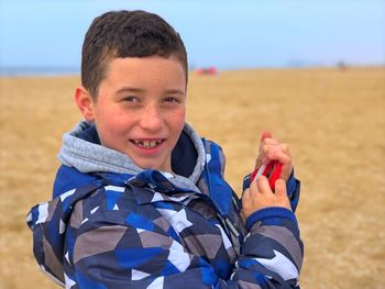 Close-up portrait of boy smiling while standing at beach during winter