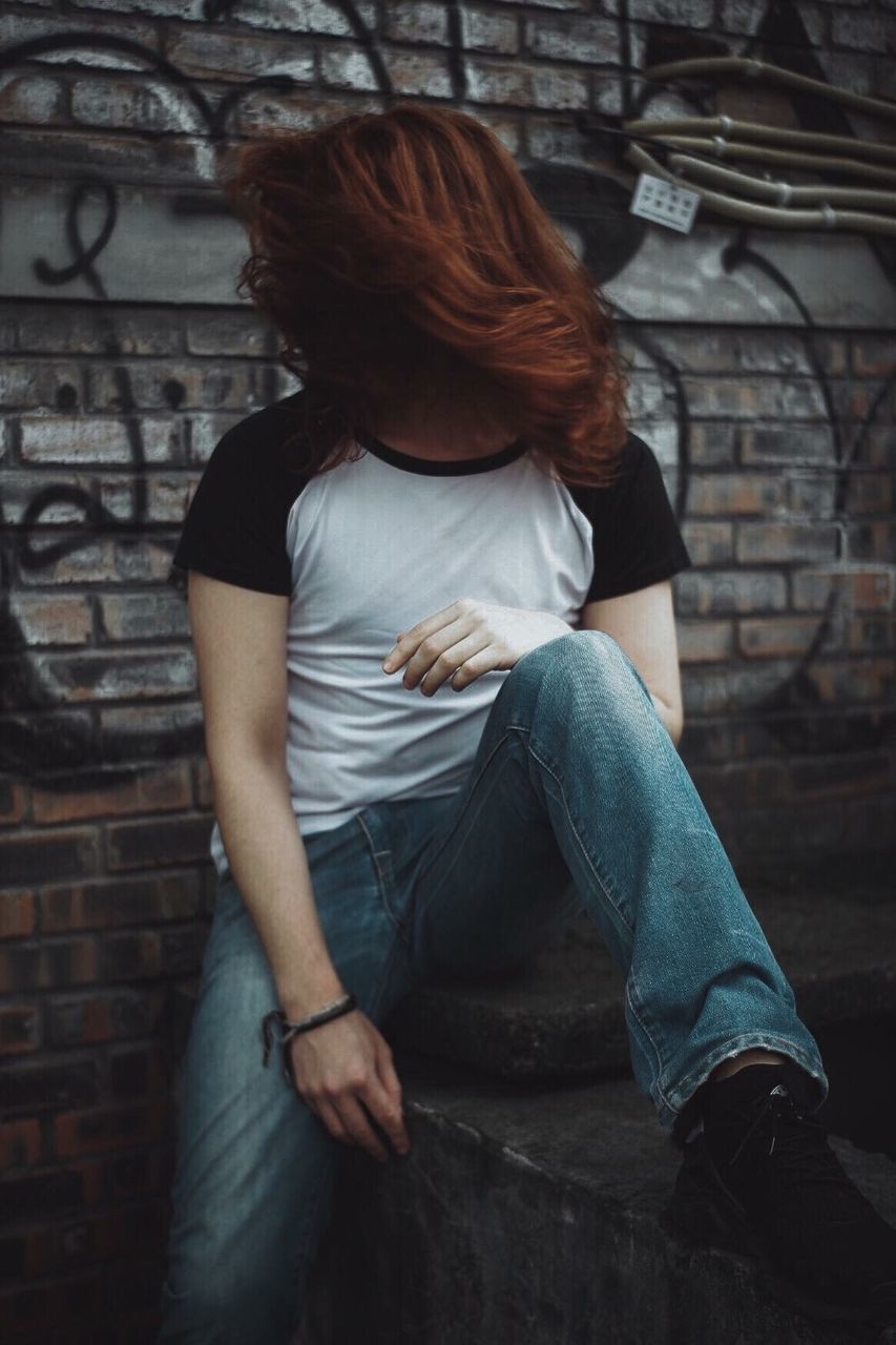 MIDSECTION OF WOMAN SITTING AGAINST WALL WITH GRAFFITI IN BACKGROUND