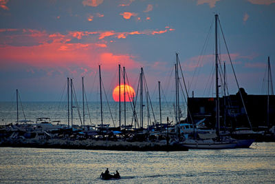 Sailboats moored in sea against sky during sunset