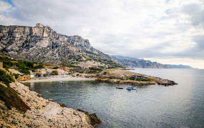 Scenic view of sea and rocky mountains against cloudy sky