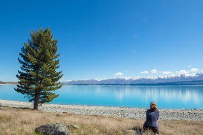 Woman sitting at lakeshore against blue sky