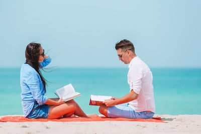 People sitting on beach by sea against clear sky