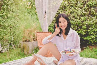 Portrait of young woman painting while sitting outdoors