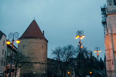 Low angle view of illuminated street light by building against sky