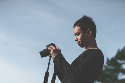 Side view of man photographing against sky