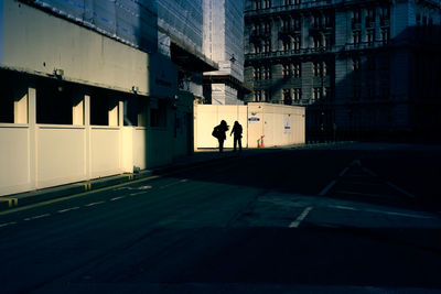 Silhouette people walking on street amidst buildings in city