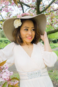 Portrait of young woman wearing hat standing against tree