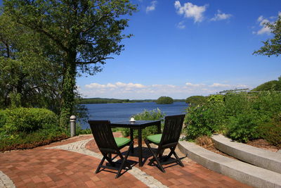 Chairs and table by lake against sky