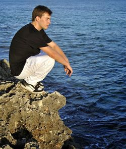 Side view of young man on rock in sea