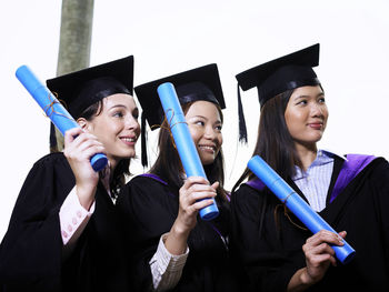 Smiling students wearing graduation gowns looking away