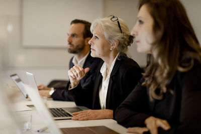 Mature businesswoman sitting with colleagues at conference table in office meeting