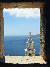 Bell tower and sea seen through window against blue sky