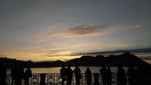 Silhouette people standing by sea against sky during sunset