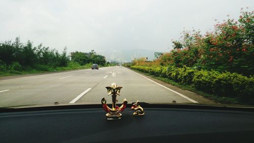 Vehicles on road along trees seen through dashboard