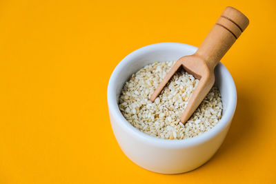 Wooden spoon with sesame seeds lies in a white mortar on a yellow background. healthy eating. keto 