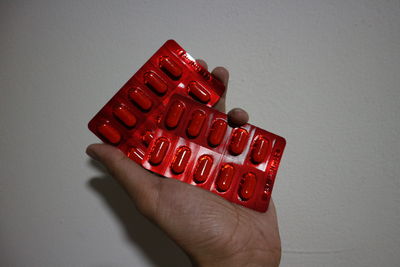 Close-up of hand holding red plastic against white background