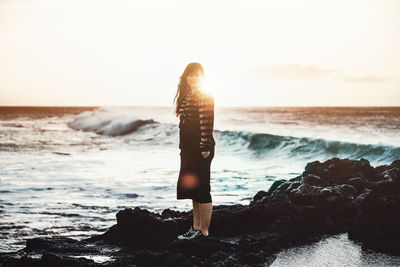 Rear view of woman standing at beach against sky