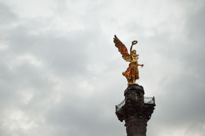 Low angle view of angel statue against cloudy sky