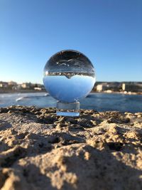 Close-up of crystal ball on beach against clear blue sky