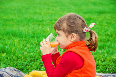 Side view of girl blowing bubbles while sitting on field