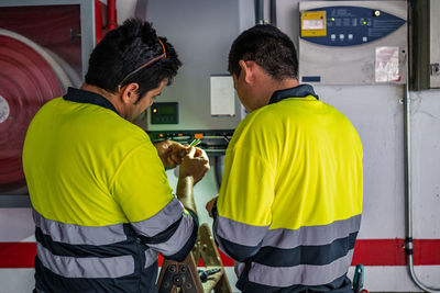 Back view of group of professional male technicians with electric tools repairing and checking equipment while working in building