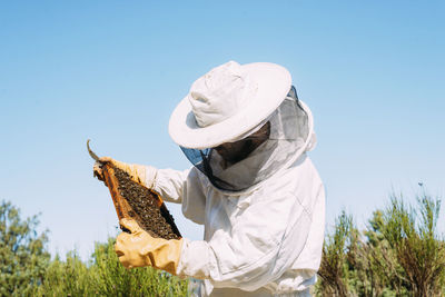 Beekeeper holding beehive against clear sky