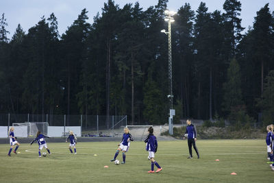 Coach looking at female athletes playing soccer on field