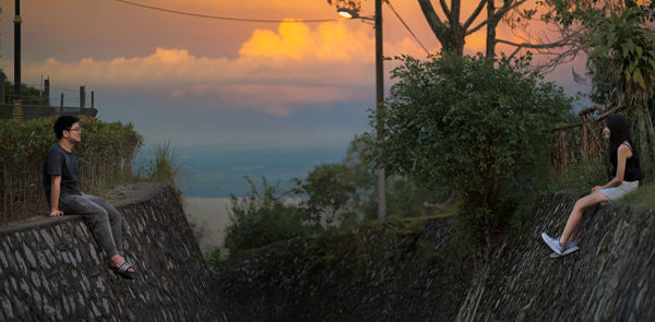 Friends sitting on surrounding wall during sunset