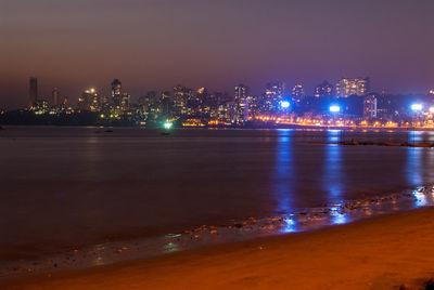 Illuminated city by sea against sky at night