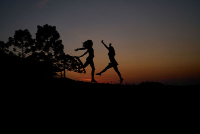 Silhouette men on landscape against sky during sunset