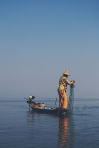 Fisherman fishing in river against clear blue sky