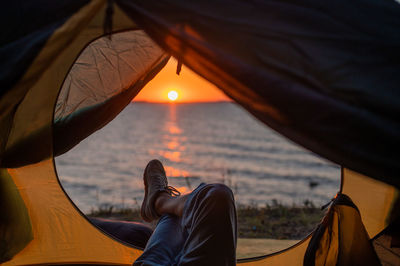 Man relaxing on tent against sky during sunset