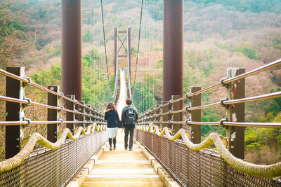 Rear view of man and woman walking on footbridge amidst trees