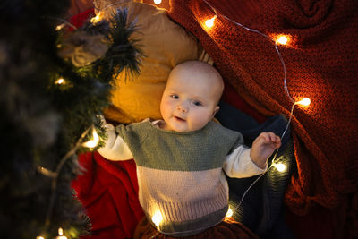 Baby 6 months in a sweater next to the christmas tree, the concept of new year and christmas
