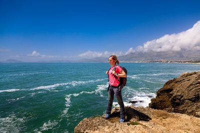 Rear view of woman standing on rock by sea against sky