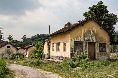 Old house amidst plants and trees against sky