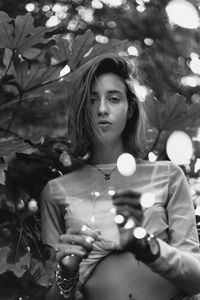 Portrait of woman holding string lights standing against plants