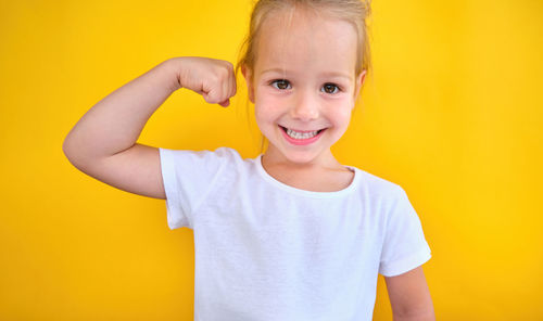 Portrait of young woman holding heart shape against yellow background