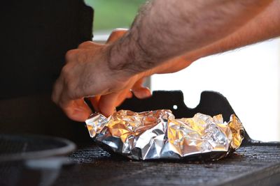 Cropped image of man wrapping food on barbecue grill