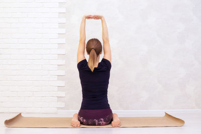 Full length of woman with arms raised against wall