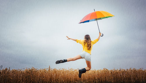 Rear view of woman holding umbrella while levitating against cloudy sky