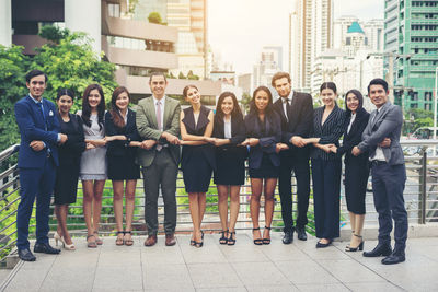 Portrait of smiling colleagues holding hands standing elevated walkway 