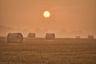 Hay bales on field against sky during sunset