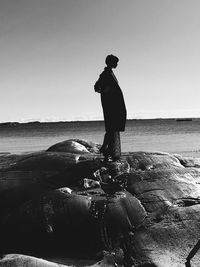 Man standing on rock at beach against clear sky