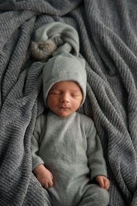 Cute newborn baby in funny a cap with a pompom sleeping on gray blanket. bed vibes