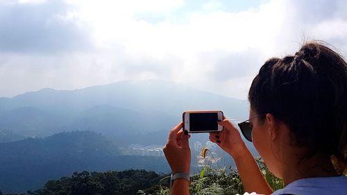 Rear view of person photographing on mountain against sky