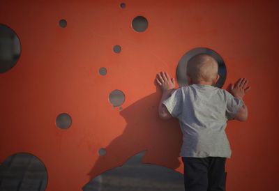 Rear view of boy standing against red wall