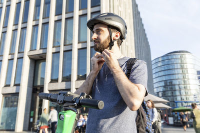 Man using e-scooter in berlin, fastening safety helmet, germany